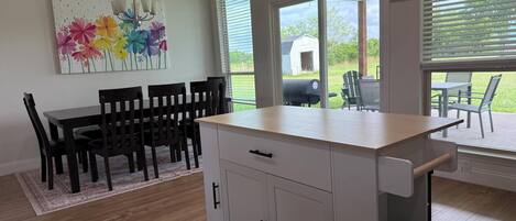 A modern kitchen with a dining area, large windows, and a view of the outdoors.