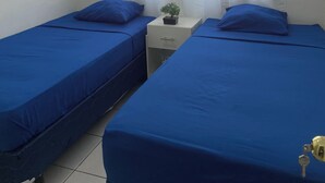 A room with two beds, a small table with a plant, and a window with sheer curtains. - Lodging with the Lopez family in Santa Ana (El salvador)