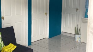 A room with two white doors, a blue wall, a white tiled floor, a black sofa with a yellow jacket, and a clock on the wall. - Lodging with the Lopez family in Santa Ana (El salvador)