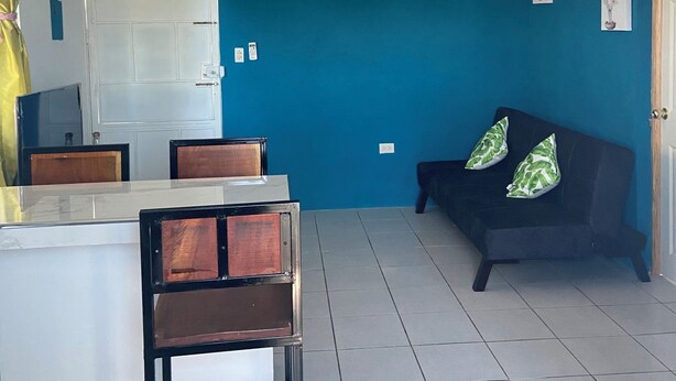 A room with a dining area, a sofa, a clock, and a door. - Lodging with the Lopez family in Santa Ana (El salvador)