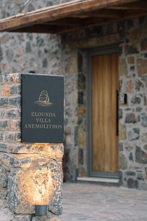 Eine Steinsäule mit einem Schild für 'Elounda Villa Anemolithos' und einer Holztür.