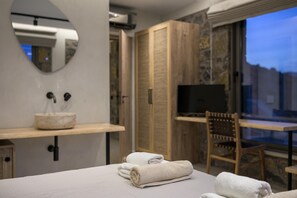 Ett hotellrum med en säng, en trästol, en tv, en spegel och ett fönster med utsikt.