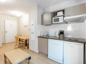 Eine kompakte Küche mit Mikrowelle, Kaffeemaschine und Geschirrspüler. Ein Esstisch mit Stühlen und einer Bank steht bereit.
