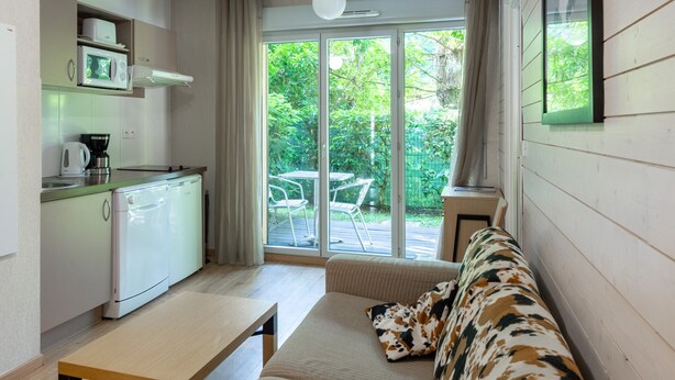 A compact kitchen with a microwave, coffee maker, and a small refrigerator. There is a dining area with a table and a sofa. A large sliding glass door leads to an outdoor patio with a table and chairs. - Bright apartment with nature view 4 people (Ax-les-Thermes)
