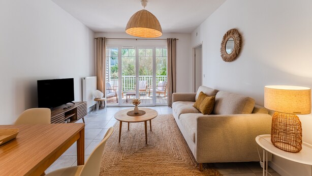 A living room with a sofa, TV, wooden table, and a balcony with outdoor furniture. - “Cocon Des Sables-Bassin d’Arcachon” Apartment with Shared Pool, Private Terrace & Wi-Fi (La Teste-de-Buch)