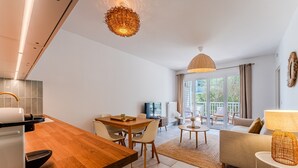 A modern kitchen with a dining area, a sofa, and a TV in the background. - “Cocon Des Sables-Bassin d’Arcachon” Apartment with Shared Pool, Private Terrace & Wi-Fi (La Teste-de-Buch)