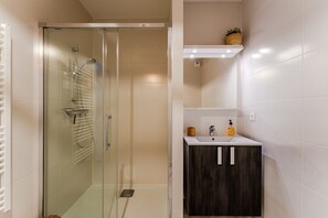 Ein modernes Badezimmer mit einer begehbaren Glasdusche, einem Holz-Waschtisch und einer weißen Fliesenwand.