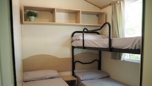A bunk bed room with a single bed, a nightstand, a shelf with a plant, and a window with curtains. - 2-bed Tuscan Mobile Home With Garden (Bucine)