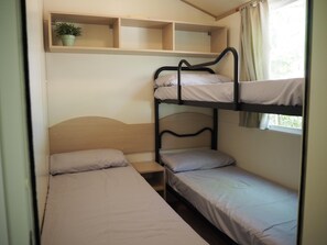 A bunk bed room with a single bed, a nightstand, a shelf with a plant, and a window with curtains. - 2-bed Tuscan Mobile Home With Garden (Bucine)