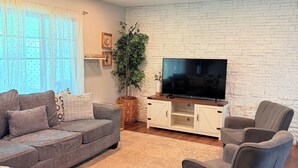 A living room with a sofa, armchair, TV, and decorative items. - Stylish house in Raleigh, sleeps 12 (Raleigh)