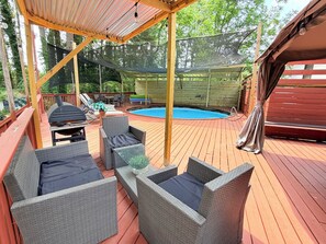 Eine überdachte Terrasse im Freien mit Korbmöbeln, einem Pool und einem Grill.