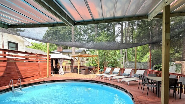 A swimming pool with a wooden deck, lounge chairs, and a covered patio area. - Stylish house in Raleigh, sleeps 12 (Raleigh)