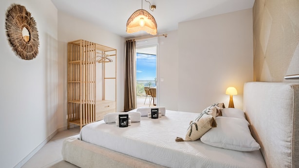 Ein modernes Schlafzimmer mit Bett, Kleiderschrank, Pendelleuchte und Blick ins Freie.