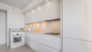 Eine moderne Küche mit weißen Schränken, einem Backofen, einer Spüle und Beleuchtung unter den Schränken.