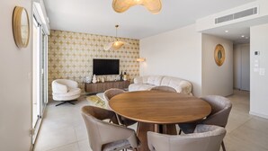 Ein modernes Wohnzimmer mit einem runden Holztisch, beigen Sofas und einem an der Wand befestigten Flachbildfernseher.