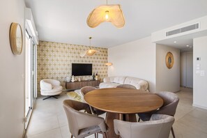 A modern living room with a round wooden dining table, beige sofas, and a flat-screen TV mounted on the wall. - 105 L l Gant in Cannes (Cannes)