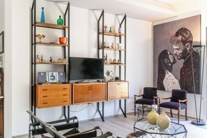 Ein Wohnzimmer mit Fernseher, Holzkredänzen, Regalen mit Dekoration, zwei Sessel und einem großen Gemälde.