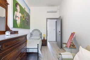 Un dormitorio con cama, cómoda, pintura y caballete.