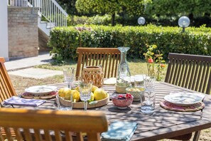 An outdoor dining table with various dishes, glasses, and a pitcher, set in a garden with a brick wall and greenery in the background. - Stunning private villa for 6 people with WIFI, A/C and veranda (Fano)