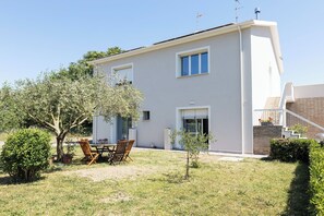 Una casa moderna de dos pisos con un patio, un árbol pequeño y una escalera que lleva a un nivel superior.