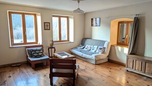 Une pièce avec un plancher en bois, un canapé, une chaise, une table et deux fenêtres.