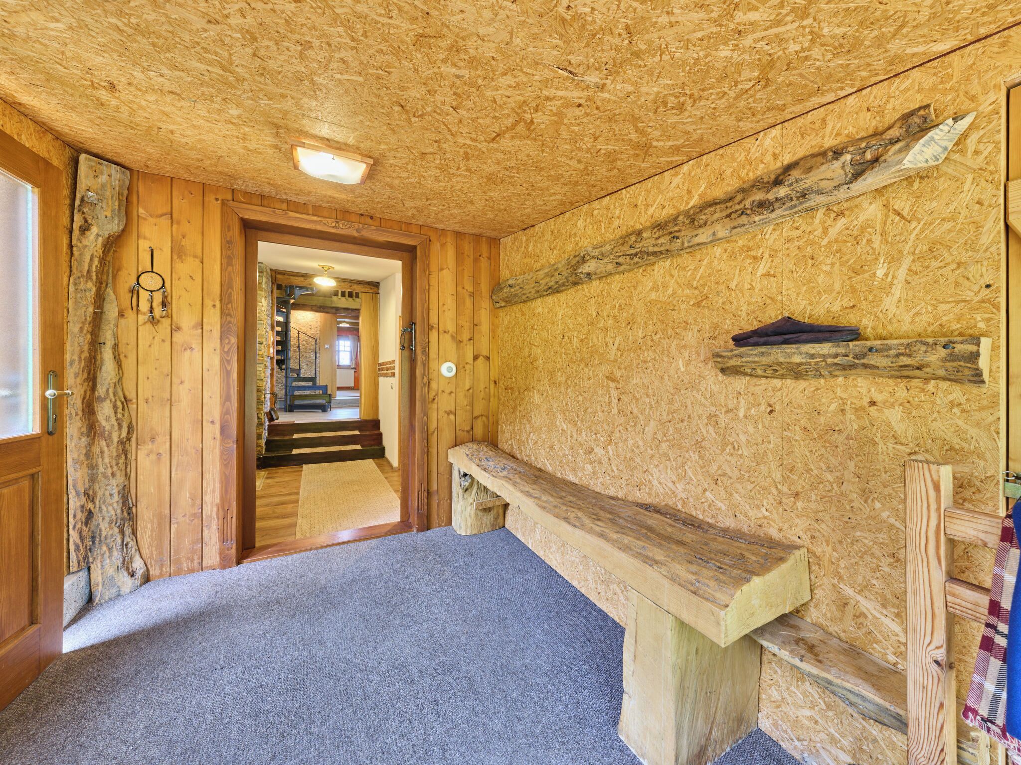 Un intérieur en bois avec un banc, un escalier et une porte donnant sur une autre pièce.