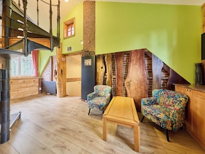 Een kamer met een houten trap, een houten tafel en twee gestreept beklede stoelen.