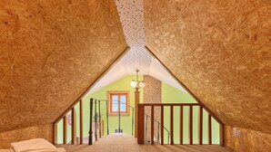 Ein Schlafzimmer mit schrägen Wänden, einer Holztreppe und Blick auf einen grünen Raum durch ein Fenster.