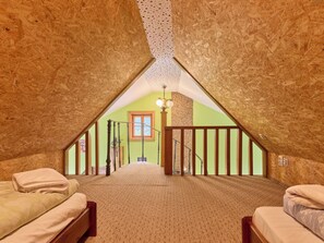 Een slaapkamer met een schuine plafond, een houten trap en uitzicht op een groene kamer door een raam.