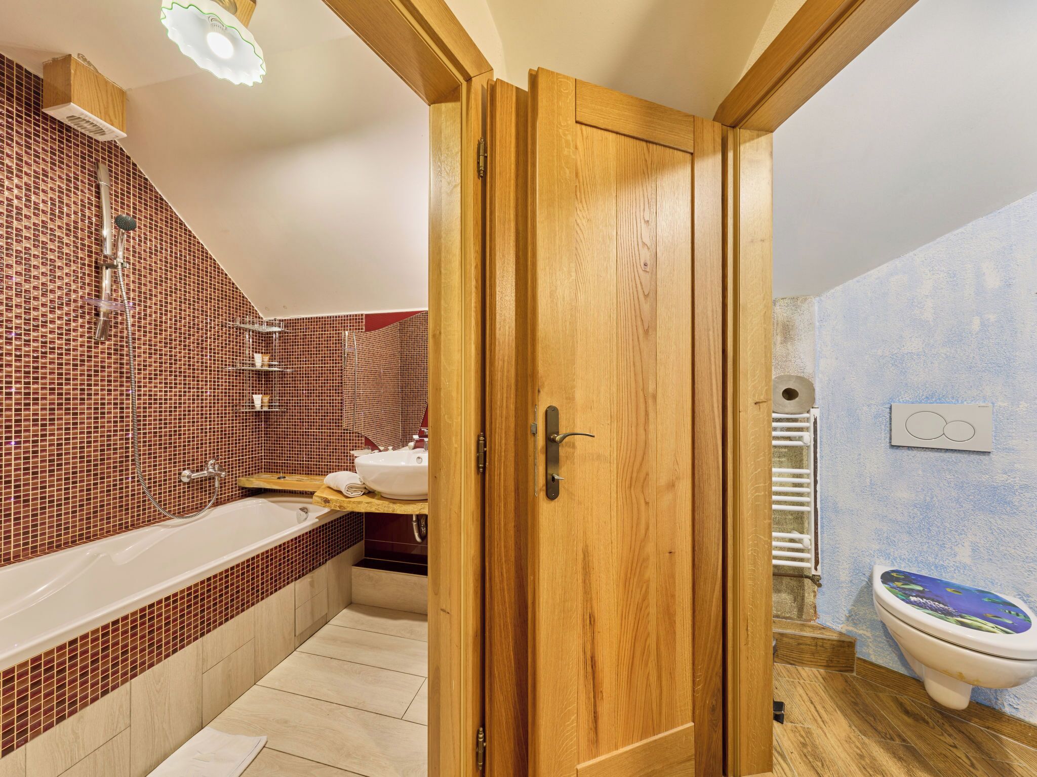 Ein Badezimmer mit Holztür, Badewanne, Toilette und Duschbereich.