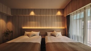 Una habitación de hotel con dos camas, un ventanal con cortinas translúcidas y una lámpara fijada a la pared.