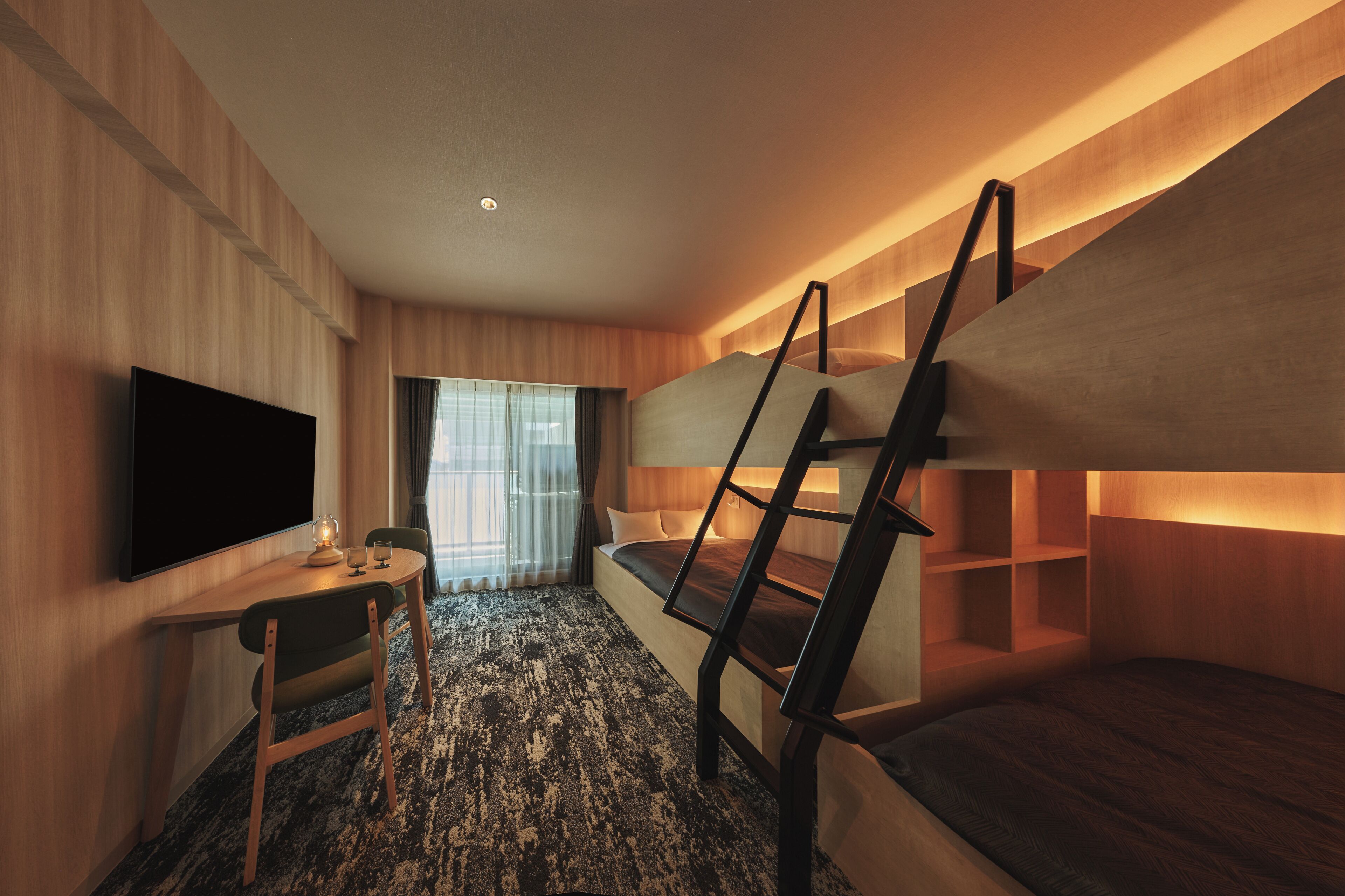 Habitación compacta con literas, un televisor de pantalla plana, una mesita con sillas y una ventana con cortinas.