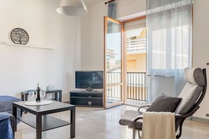 Uma sala de estar moderna com televisão, mesa de jantar, sofá e uma poltrona.