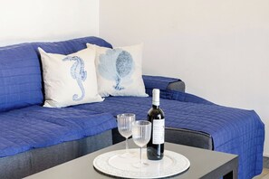 Una cama con ropa de cama azul, dos almohadas con diseños de caballitos de mar, una botella de vino y dos copas sobre una mesa.