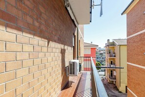 Um beco estreito com paredes de tijolo, um pequeno aparelho de ar condicionado e um corrimão de metal.