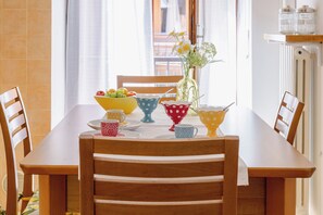 Un tavolo da pranzo con sedie, un vaso con fiori, una ciotola di frutta e tazze a pois.