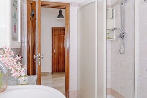 Un bagno con doccia, lavandino, specchio e una porta che dà su un'altra stanza.