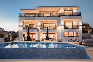 Ein modernes, mehrgeschossiges Haus mit Swimmingpool, Sitzgelegenheiten im Freien und einem gut beleuchteten Eingang.