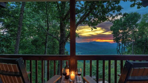 Eine Holzdielen-Terrasse mit zwei Stühlen, einem Tisch, einer Kerze und zwei Weingläsern.