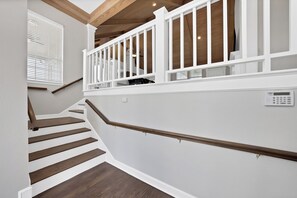 Eine Treppe mit Holzbeschlägen und weißen Geländern, die zu einer Zwischenebene mit weißer Wand und Decke mit freiliegenden Holzbalken führt.