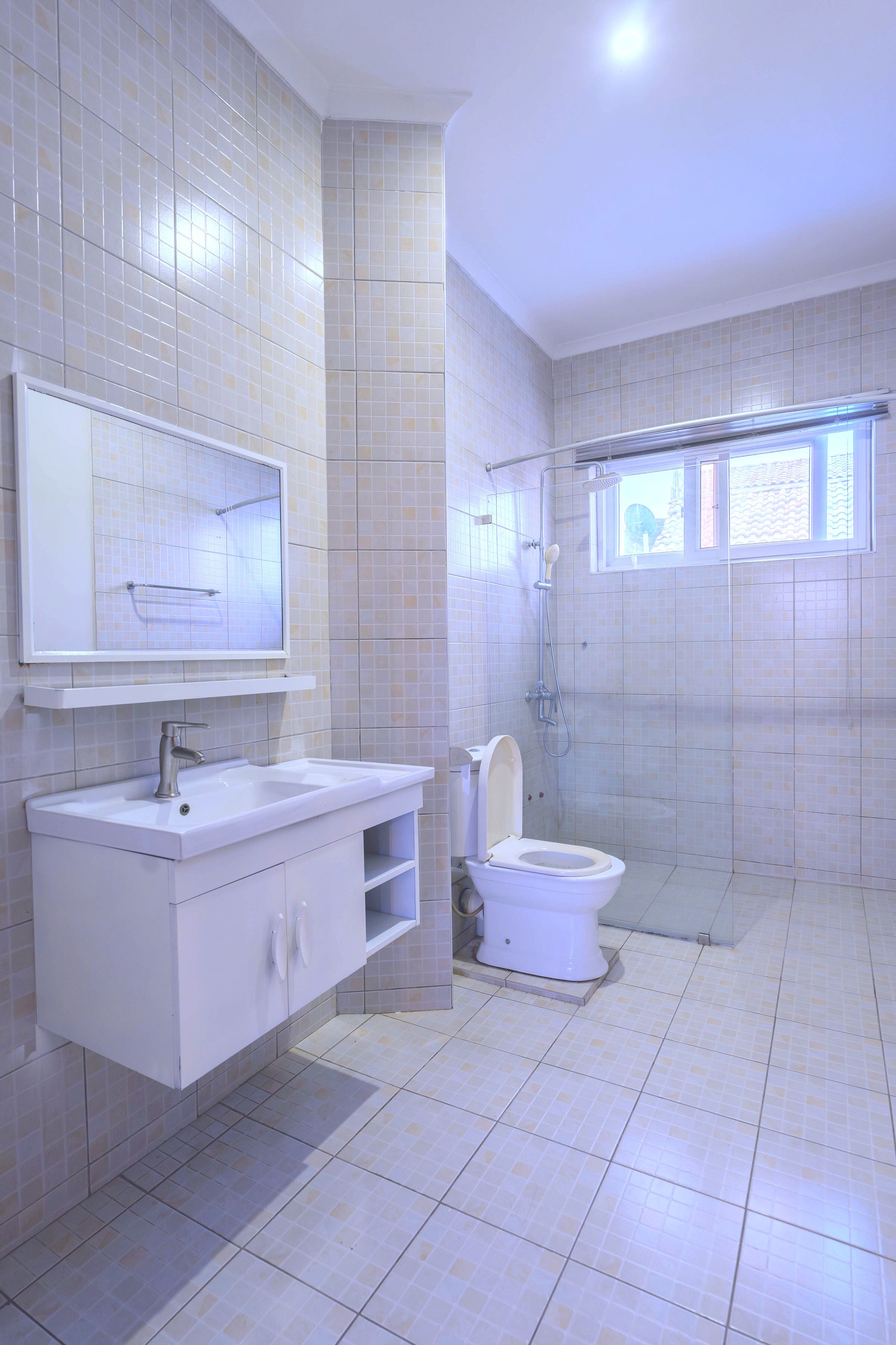 A bathroom with a sink, mirror, toilet, shower, and a window.