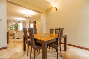 Un comedor con una mesa rectangular rodeada de sillas, una araña y vistas a una sala de estar con un sofá y una ventana.
