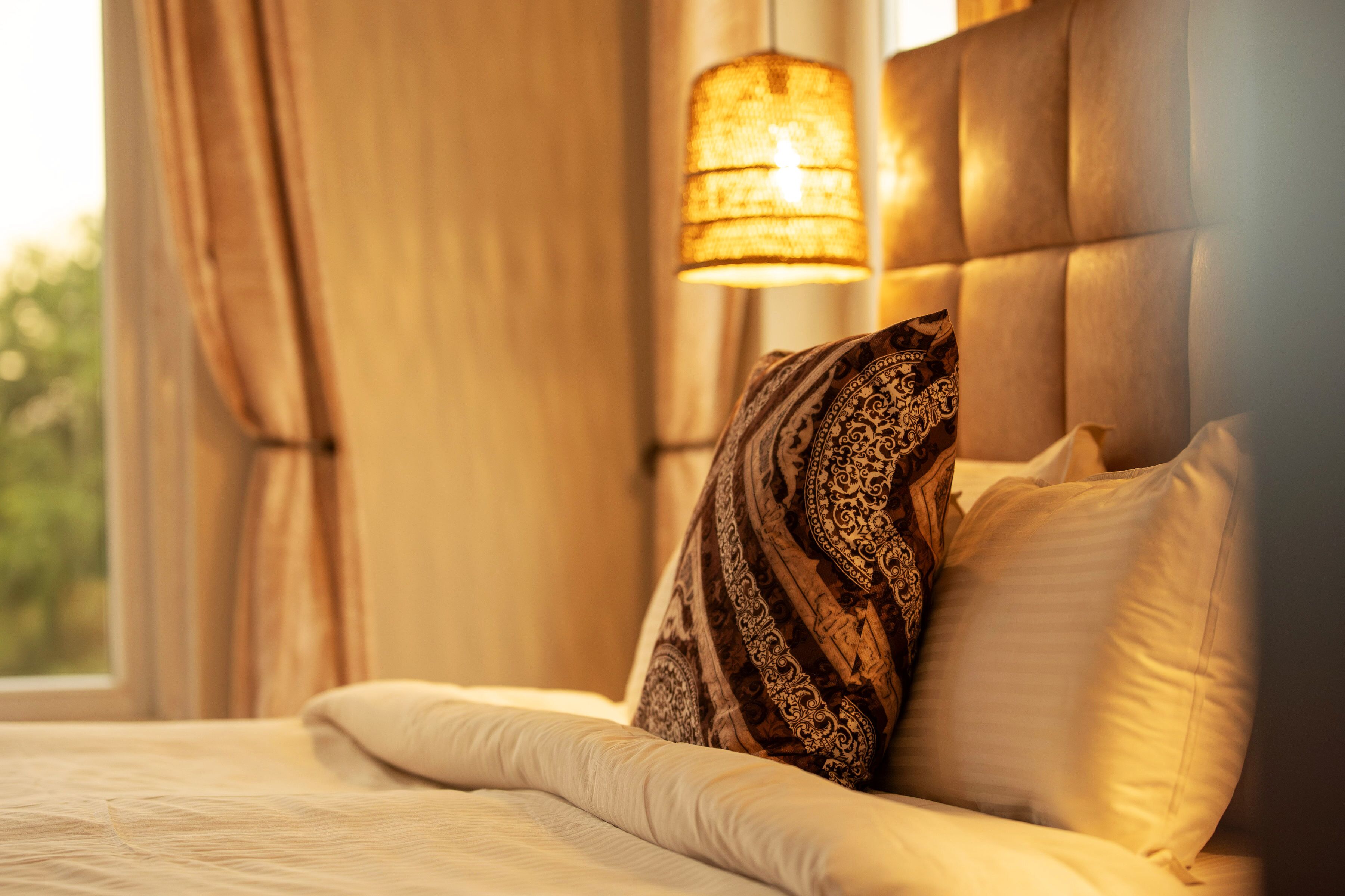 A bed with patterned pillows, a headboard, and a hanging lamp.