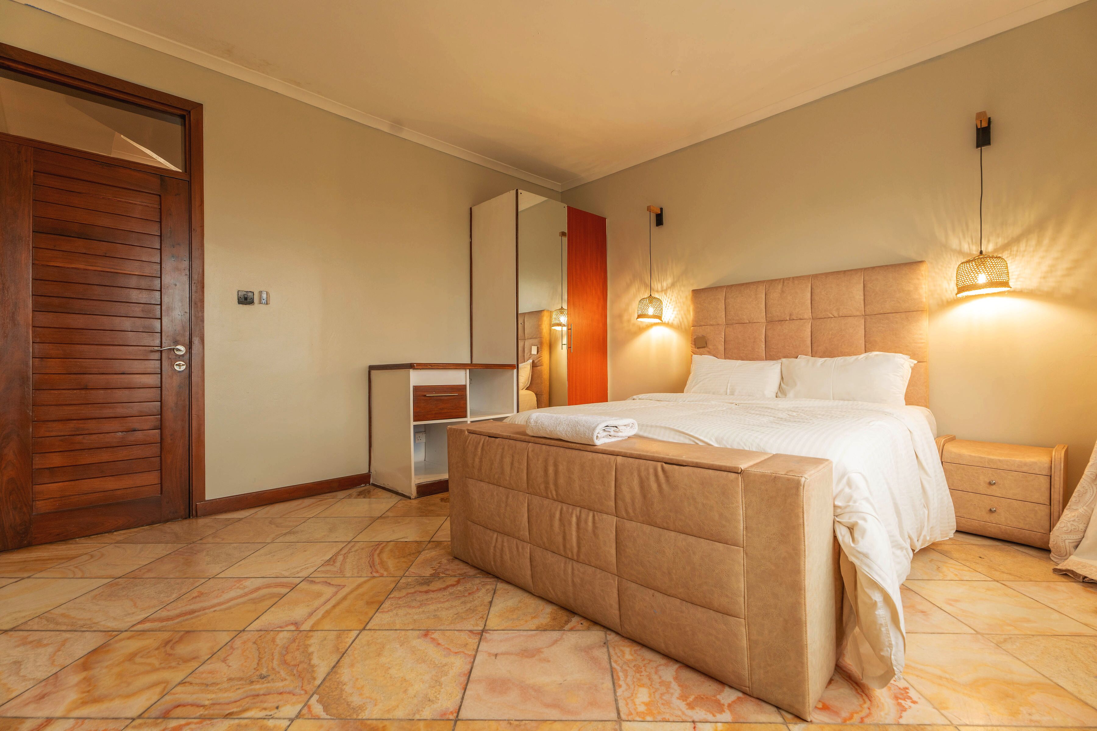 Un dormitorio con una cama grande, una puerta de madera, una mesita de noche y un buró.
