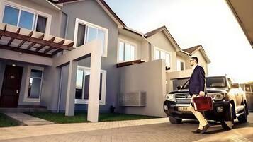 Ett modernt hus med en uppfart, en svart SUV och en person som går förbi med en portfölj.