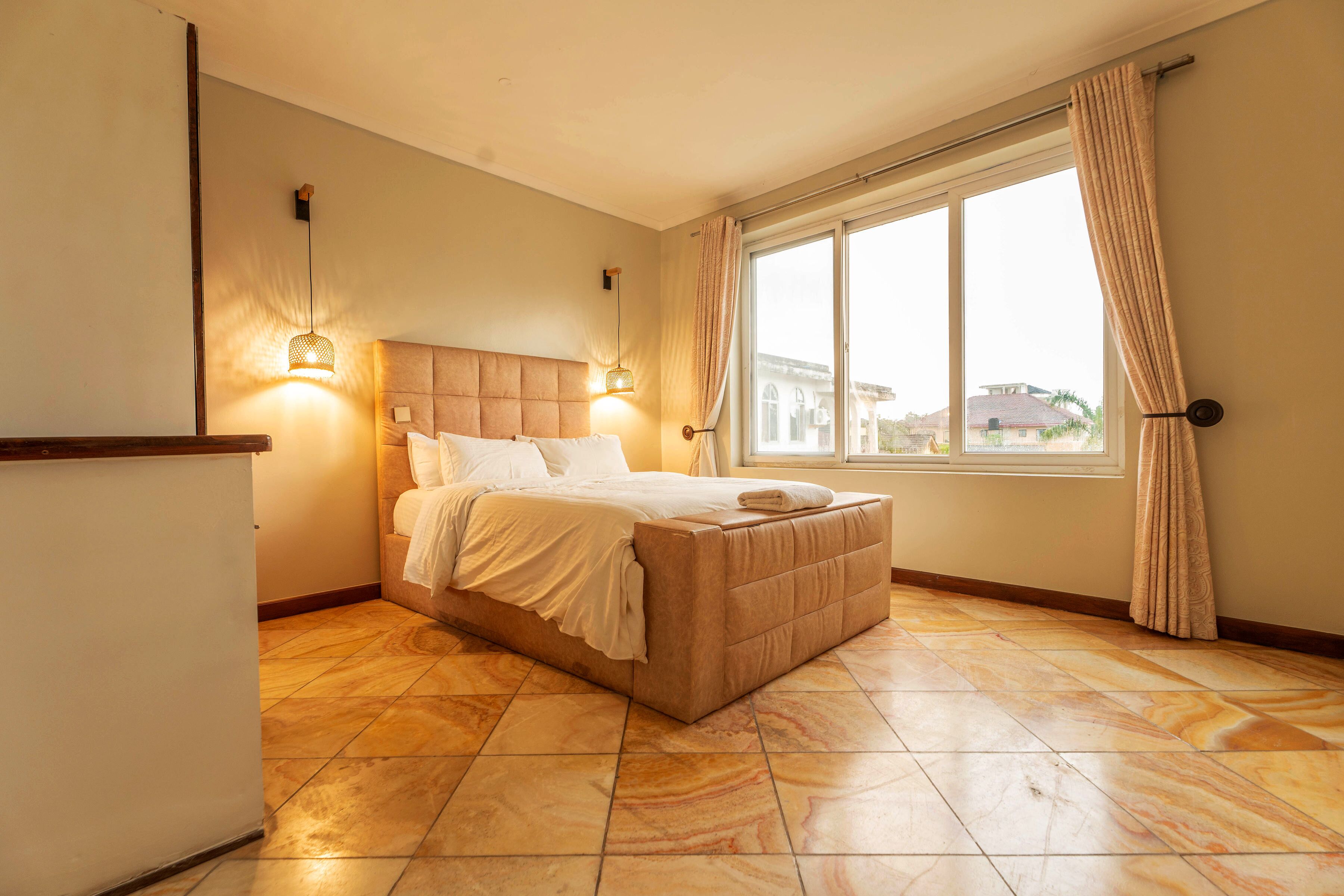 A bedroom with a bed, a window with curtains, and a wall-mounted light fixture.