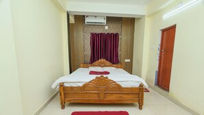 A bedroom with a wooden bed, a red rug, a ceiling fan, and a door. - Silver Residency (Bhubaneshwar)