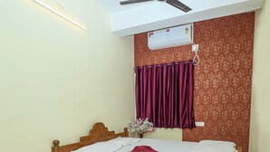 A bedroom with a bed, a ceiling fan, an air conditioner, a red rug, and patterned wallpaper. - Silver Residency (Bhubaneshwar)