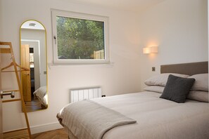 Un dormitorio con una cama, una ventana, un espejo, una lámpara de noche y una escalera de madera.