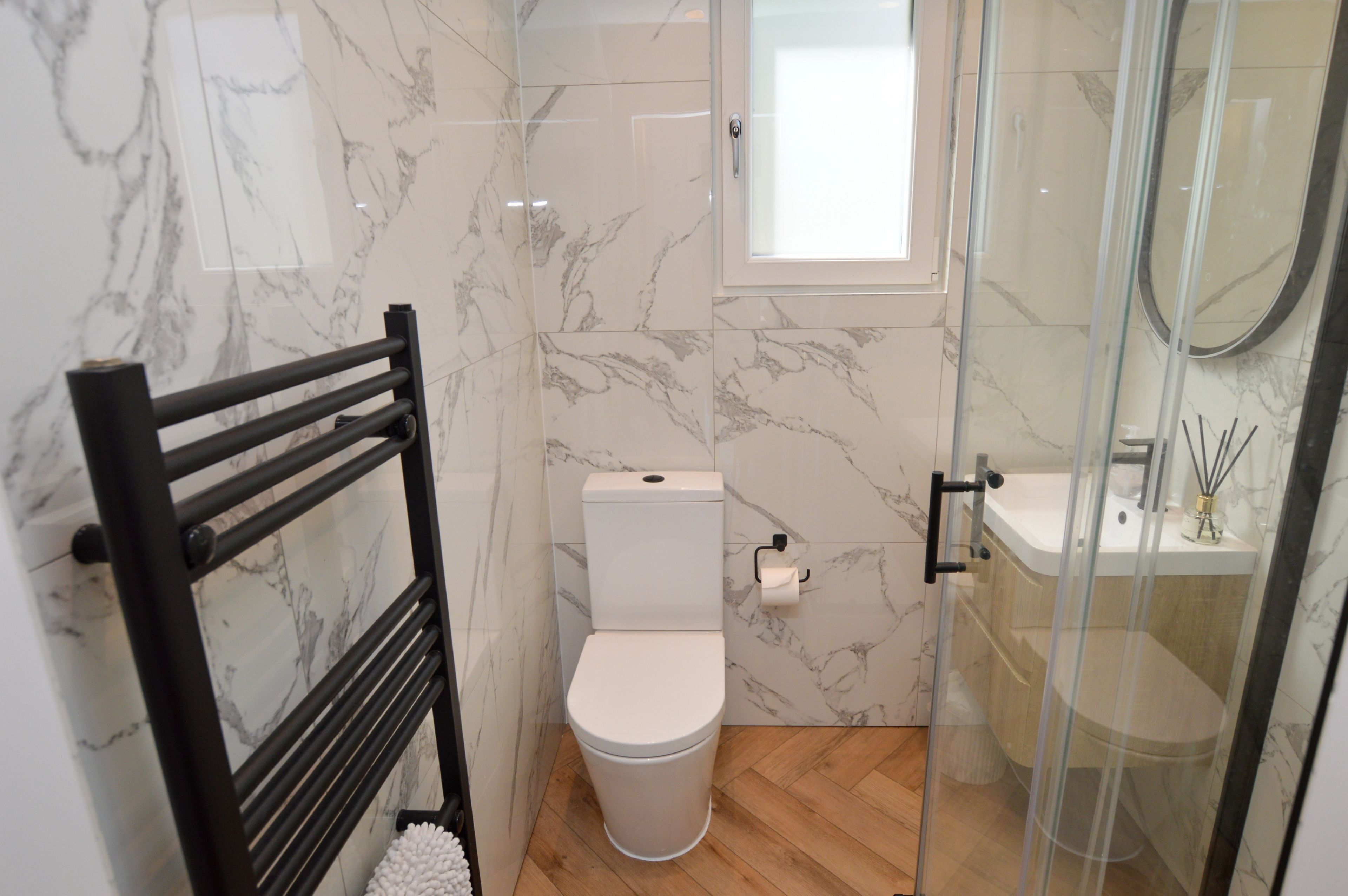A bathroom with a toilet, a glass shower enclosure, a sink, and a towel rack.